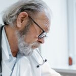senior-doctor-with-glasses-and-stethoscope-focused-on-work-i