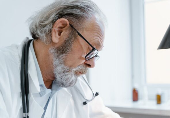 senior-doctor-with-glasses-and-stethoscope-focused-on-work-i